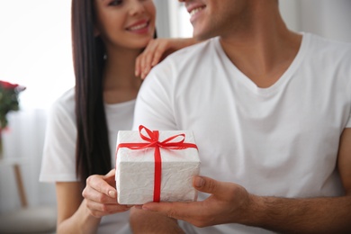 Man presenting gift to his beloved woman at home, focus on box. Valentine's day celebration