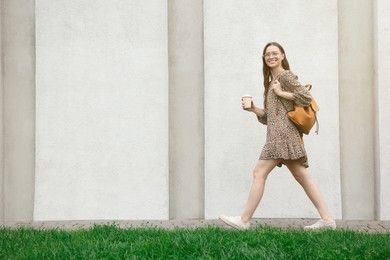 Young woman with cup of drink walking near stone wall outdoors, space for text