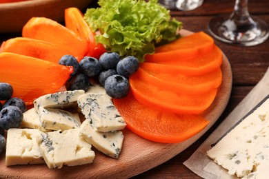 Photo of Delicious persimmon, blue cheese and blueberries on wooden table, closeup