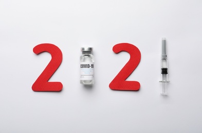 Paper numbers, syringe and vial with coronavirus vaccine forming 2021 on white background, flat lay