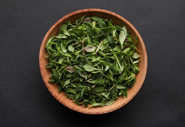 Wooden bowl of fresh green thyme leaves on dark background, top view