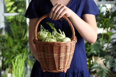 Woman holding wicker basket with ripe kohlrabi plants outdoors, closeup