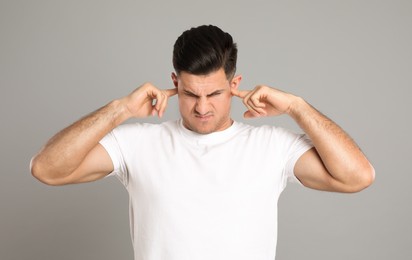 Emotional man covering ears with fingers on grey background
