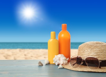 Different bottles of skin sun protection body cream and beach accessories on light blue wooden table against seascape. Space for design