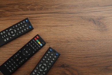 Modern tv remote controls on wooden table, flat lay. Space for text