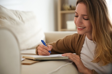 Happy woman writing letter on sofa at home