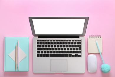 Modern laptop and office stationery on pink background, flat lay