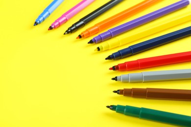 Many colorful markers on yellow background, space for text. School stationery