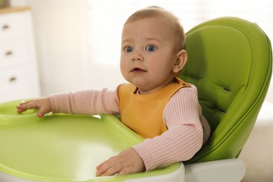 Cute little baby wearing bib in highchair indoors