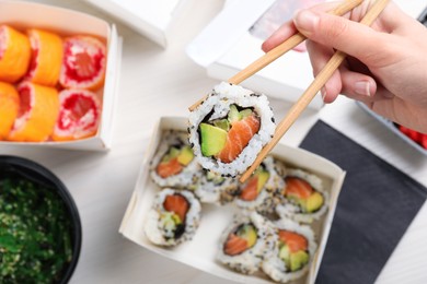 Woman eating sushi rolls with chopsticks at white table, top view