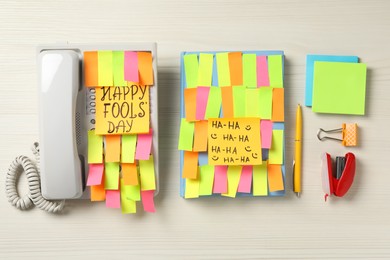 Corded phone and notebook covered with sticky notes on wooden table, flat lay. April fool's day celebration