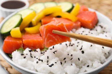 Photo of Chopsticks with salmon over delicious poke bowl , closeup