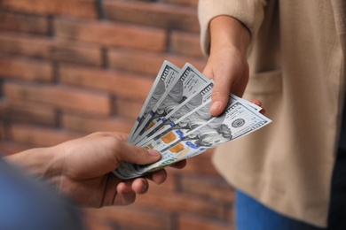 Man giving woman American money near brick wall, closeup