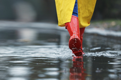 Woman in rubber boots walking outdoors on rainy day, closeup. Space for text