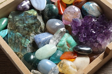 Box with different beautiful gemstones on table, closeup
