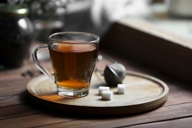 Tray with cup of freshly brewed tea and sugar cubes on wooden table indoors