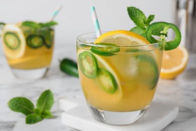 Photo of Spicy cocktail with jalapeno, lemon and mint on white marble table, closeup