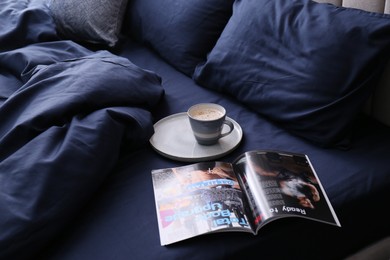 Open magazine and cup of coffee on bed with stylish silky linens