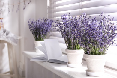 Photo of Beautiful lavender flowers and book on window sill indoors. Space for text