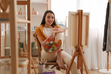 Beautiful young woman with drawing tools near easel at home