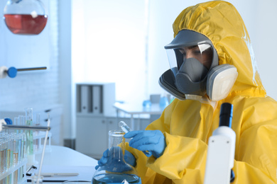 Scientist in chemical protective suit pouring reagent into flask at laboratory. Virus research