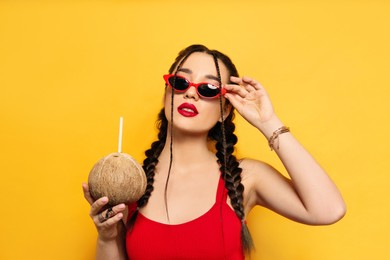 Photo of Young woman with fresh coconut on yellow background. Exotic fruit
