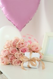 Photo of Beautiful bouquet of roses, gift and balloons on white table. Happy birthday greetings