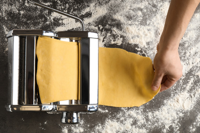 Woman preparing dough with pasta maker machine at grey table, top view