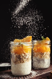 Photo of Powdering tasty peach dessert with icing sugar on black background