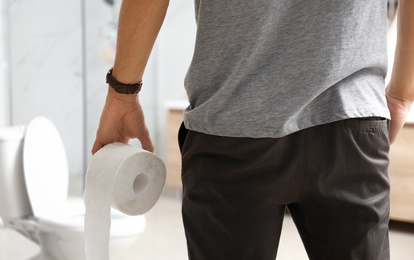 Man with paper roll near toilet bowl in bathroom, closeup