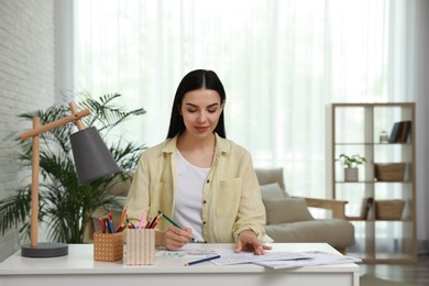 Young woman coloring antistress page at desk indoors