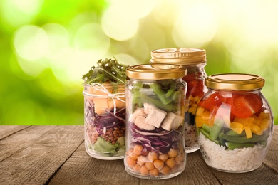 Jars with different healthy meals on wooden table against blurred background
