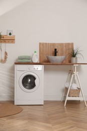 Laundry room interior with modern washing machine and stylish vessel sink on wooden countertop
