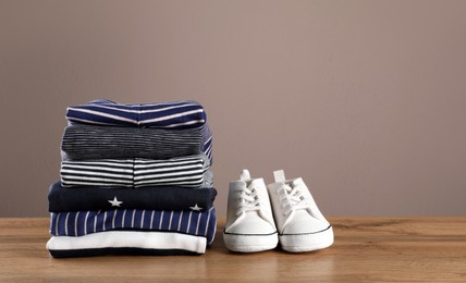 Stack of baby boy's clothes and shoes on wooden table against brown background, space for text