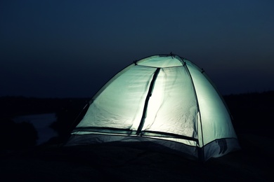 Small camping tent glowing in twilight outdoors. Space for text