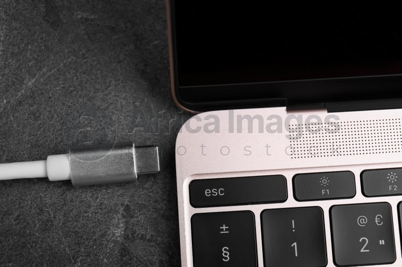 USB cable with type C connector and laptop on grey table, closeup