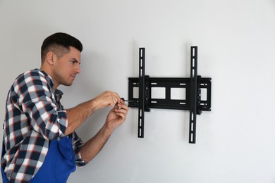 Professional technician with screwdriver installing TV bracket on wall indoors