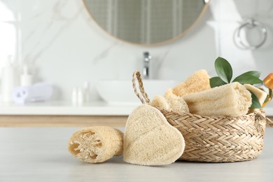 Photo of Natural loofah sponges near wicker basket on table in bathroom. Space for text