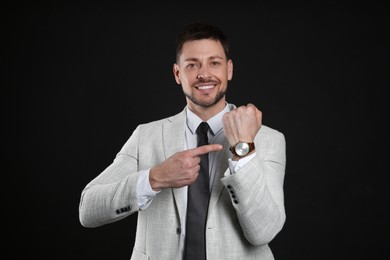 Happy businessman pointing on wristwatch against black background. Time management