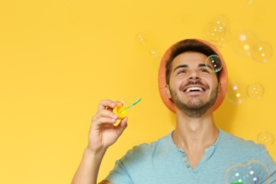 Photo of Young man blowing soap bubbles on color background. Space for text