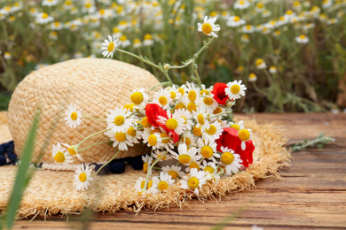 Bouquet of poppies and chamomiles with straw hat on wooden table outdoors