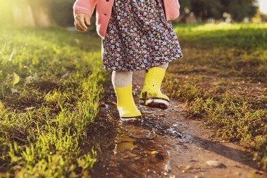 Little girl wearing rubber boots walking in puddle outdoors, closeup