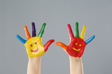 Kid with smiling faces drawn on palms against grey background, closeup