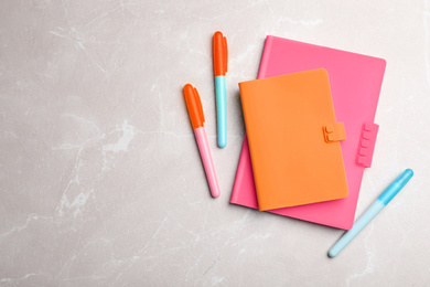 Stylish pink and orange notebooks, pens on marble table, flat lay. Space for text