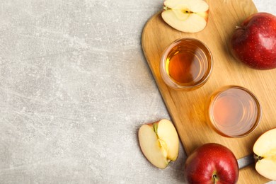 Delicious cider and ripe red apples on light grey table, flat lay. Space for text