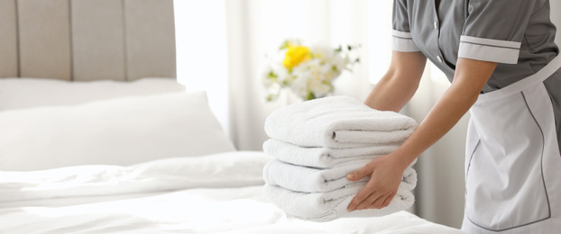 Young chambermaid putting stack of fresh towels in bedroom, closeup view with space for text. Banner design
