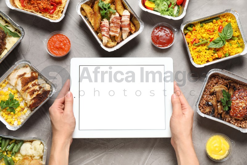 Top view of woman holding tablet over grey table with lunchboxes, mockup for design. Healthy food delivery