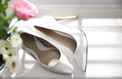 Pair of white high heel shoes and wedding bouquet on windowsill, top view