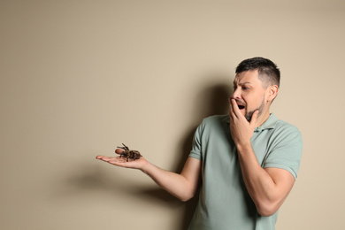 Photo of Scared man holding tarantula on beige background, space for text. Arachnophobia (fear of spiders)