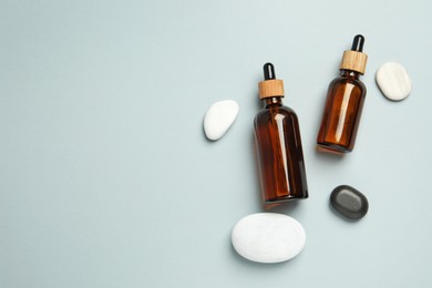 Flat lay composition with bottles of face serum and spa stones on light grey background. Space for text